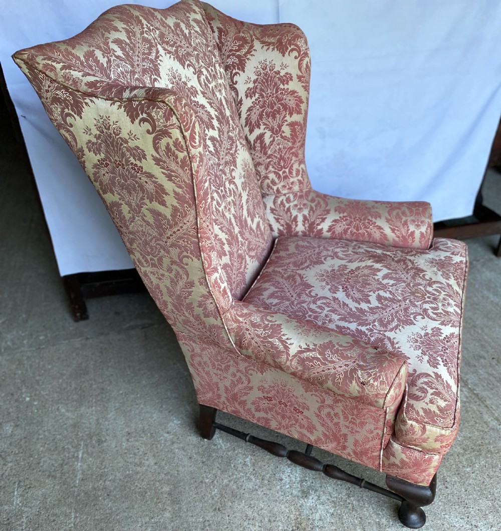A generous winged armchair upholstered in a rose pink and cream floral damask fabric with turned wooden front feet. View II