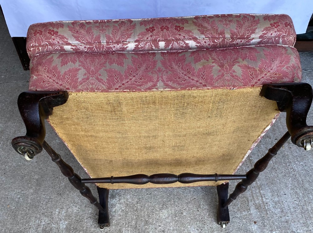 A generous winged armchair upholstered in a rose pink and cream floral damask fabric with turned wooden front feet. View IV