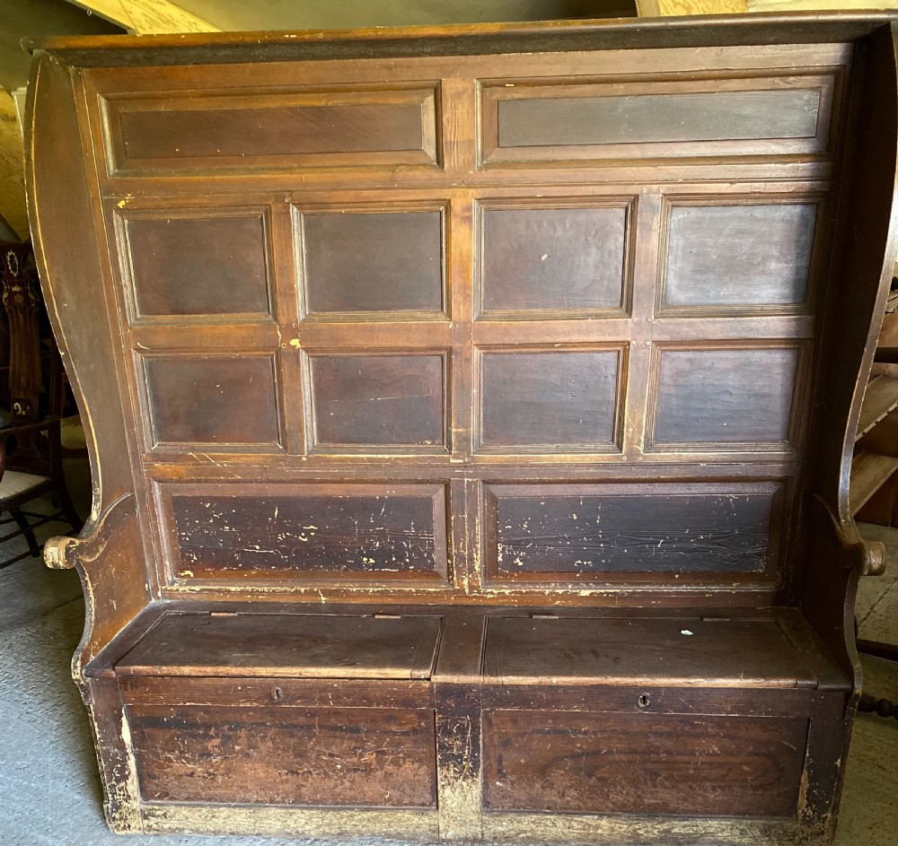 A large 19th-century high-back wooden settle featuring a multi-panelled back, winged draught sides, dark distressed finish, and a hinged seat box base.