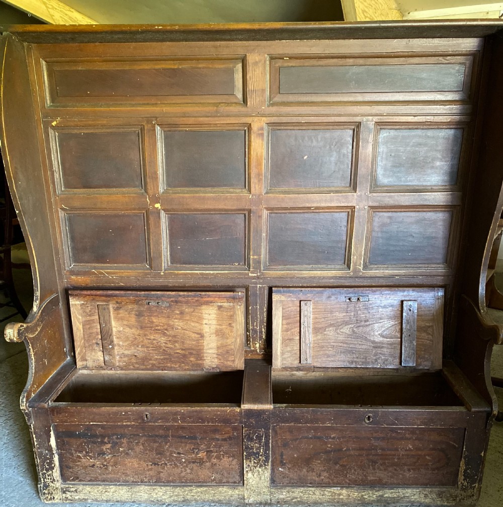 A large 19th-century high-back wooden settle featuring a multi-panelled back, winged draught sides, dark distressed finish, and a hinged seat box base. View V