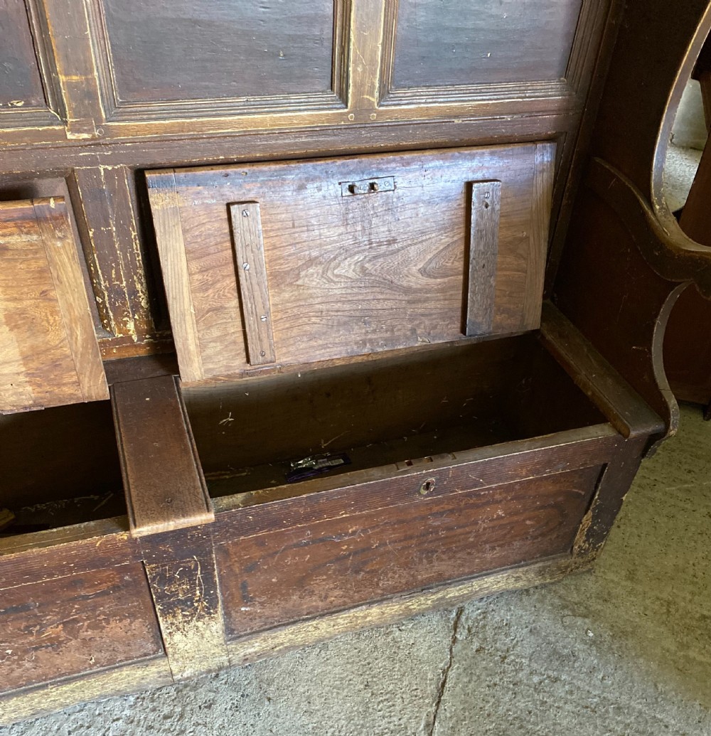A large 19th-century high-back wooden settle featuring a multi-panelled back, winged draught sides, dark distressed finish, and a hinged seat box base. View VI