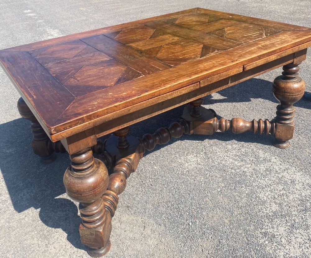 An 18th century Spanish fruitwood refectory dining table featuring a geometric parquet tabletop, draw-leaf extension panels, turned baluster legs, and a carved central stretcher. View IV