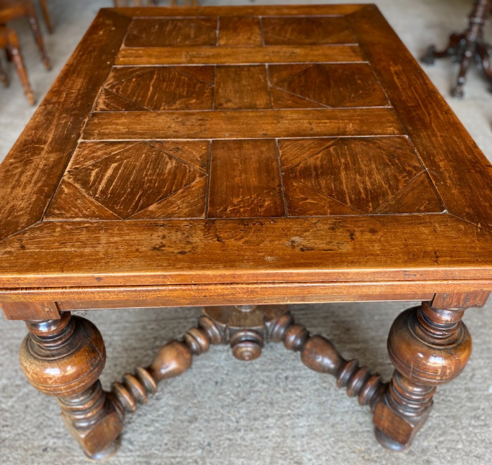 An 18th century Spanish fruitwood refectory dining table featuring a geometric parquet tabletop, draw-leaf extension panels, turned baluster legs, and a carved central stretcher. View IX