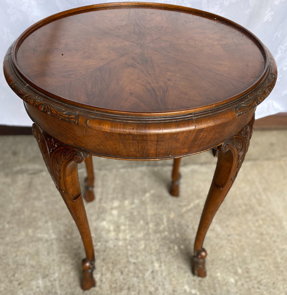 A circular antique walnut occasional table with quartered top veneer, carved apron details, and elegant cabriole legs ending in scroll feet.