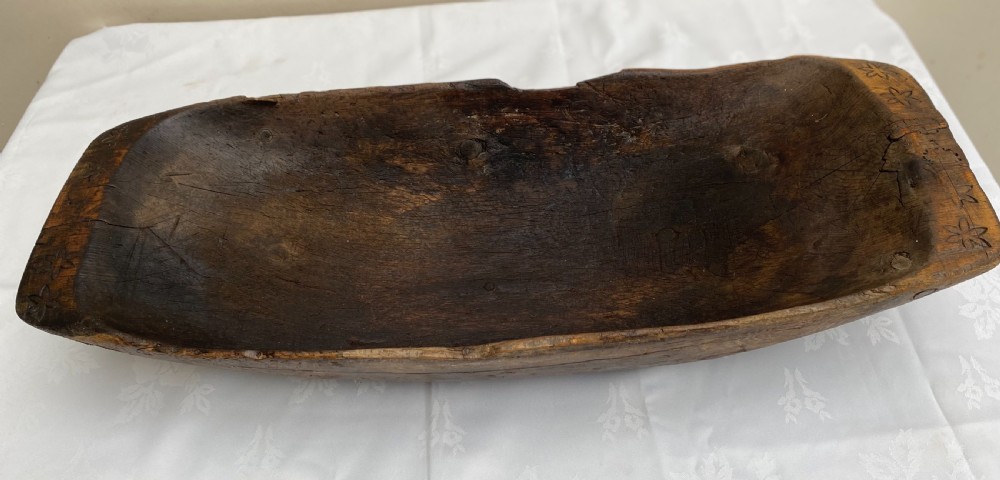 A long hand-carved dark wood bowl featuring incised star motifs on the raised rim handles and a hollowed interior.