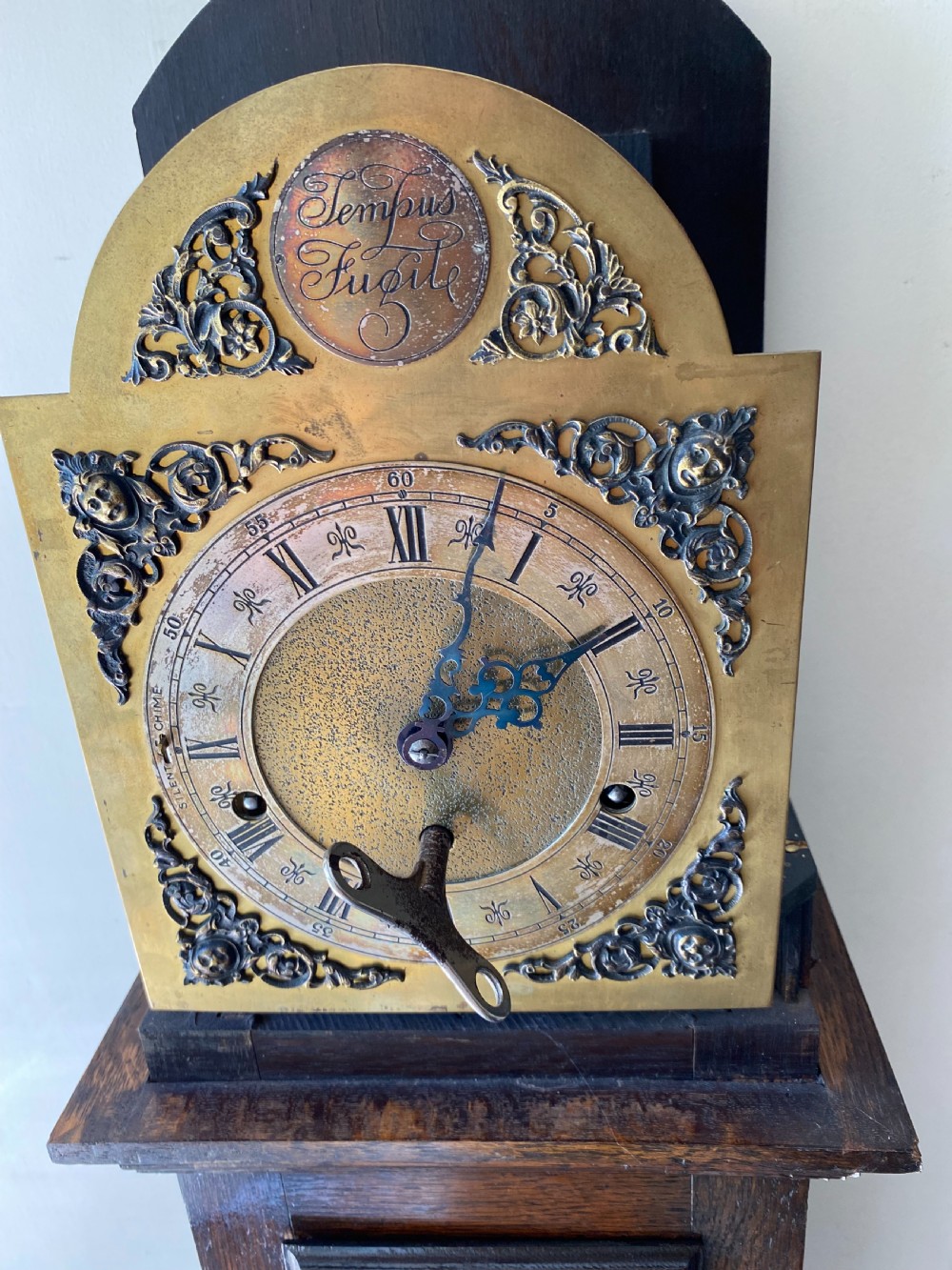 A dark oak Jacobean style grandmother clock featuring barley twist columns, geometric door panel mouldings, an arched hood, and an ornate brass dial. View II