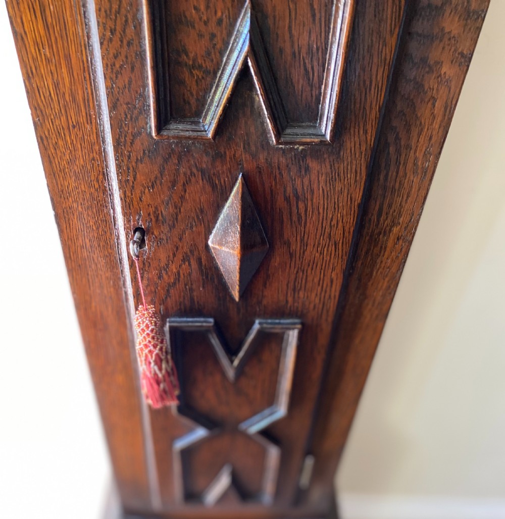 A dark oak Jacobean style grandmother clock featuring barley twist columns, geometric door panel mouldings, an arched hood, and an ornate brass dial. View IV