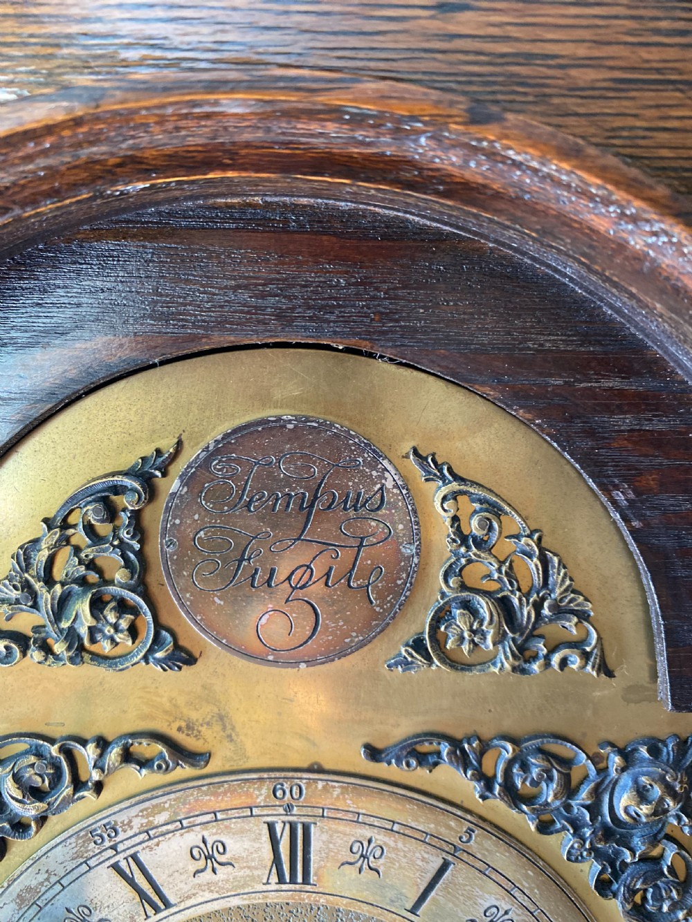 A dark oak Jacobean style grandmother clock featuring barley twist columns, geometric door panel mouldings, an arched hood, and an ornate brass dial. View VI