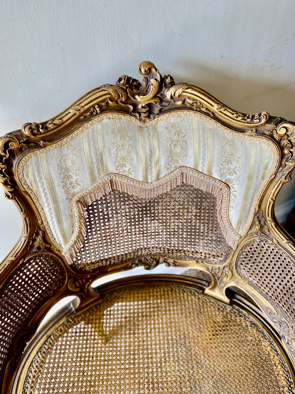 A 19th-century French giltwood bergere armchair featuring a carved ornate frame, woven cane seat and side panels, and a cream silk upholstered back section with tassel trim. View II