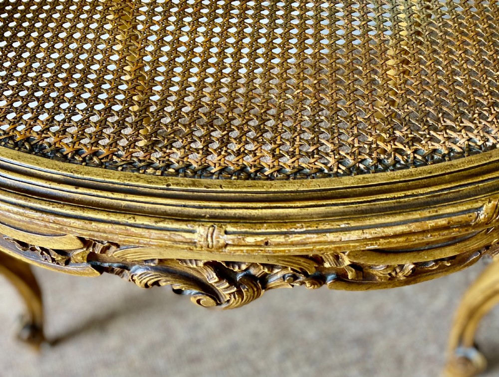A 19th-century French giltwood bergere armchair featuring a carved ornate frame, woven cane seat and side panels, and a cream silk upholstered back section with tassel trim. View VII