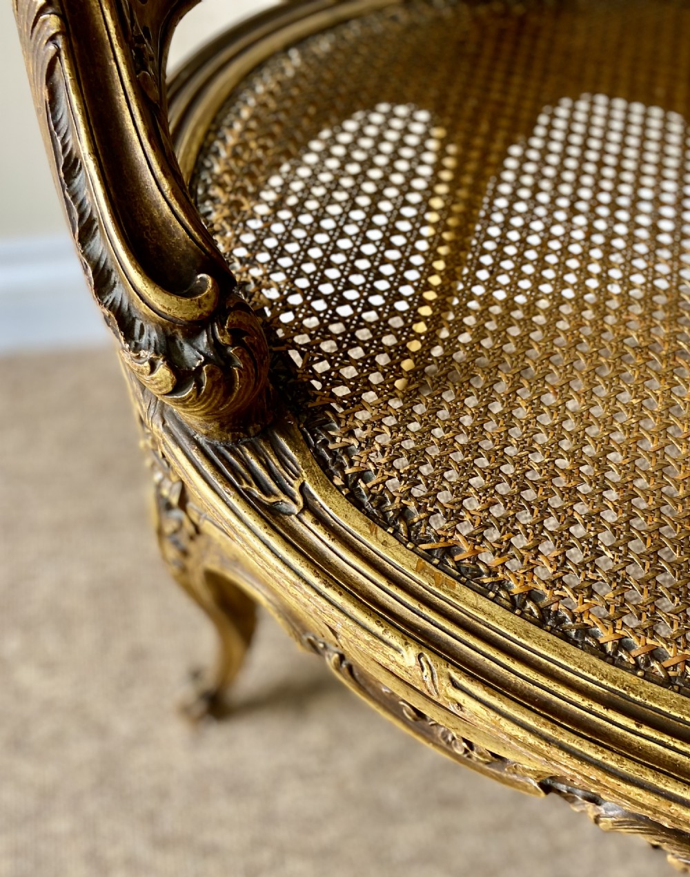 A 19th-century French giltwood bergere armchair featuring a carved ornate frame, woven cane seat and side panels, and a cream silk upholstered back section with tassel trim. View IX