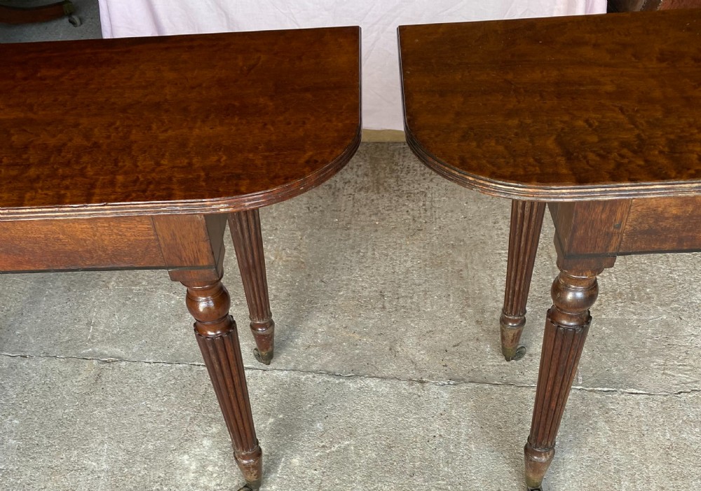 A pair of Regency mahogany console tables featuring rounded tops, reeded legs, and brass castors on a concrete surface. View III