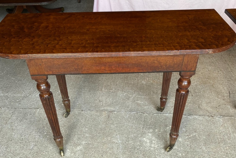 A pair of Regency mahogany console tables featuring rounded tops, reeded legs, and brass castors on a concrete surface. View IV