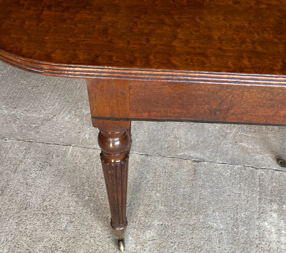 A pair of Regency mahogany console tables featuring rounded tops, reeded legs, and brass castors on a concrete surface. View V