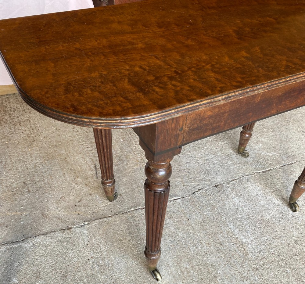 A pair of Regency mahogany console tables featuring rounded tops, reeded legs, and brass castors on a concrete surface. View VI