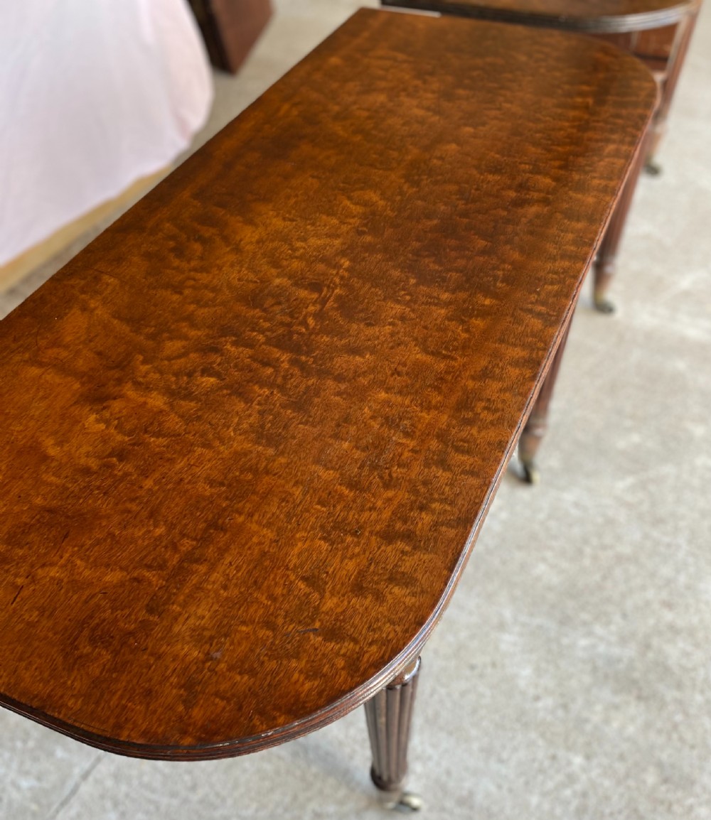 A pair of Regency mahogany console tables featuring rounded tops, reeded legs, and brass castors on a concrete surface. View VII
