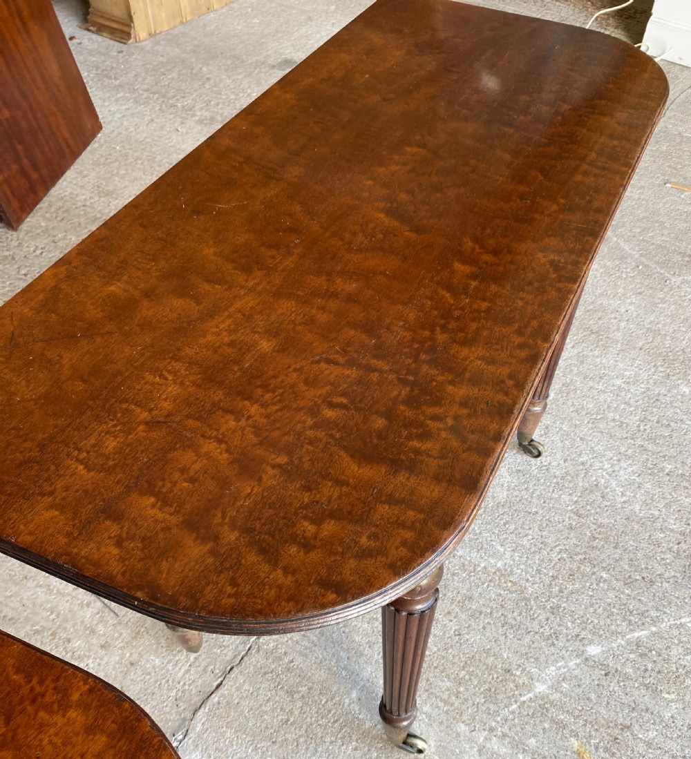 A pair of Regency mahogany console tables featuring rounded tops, reeded legs, and brass castors on a concrete surface. View VIII