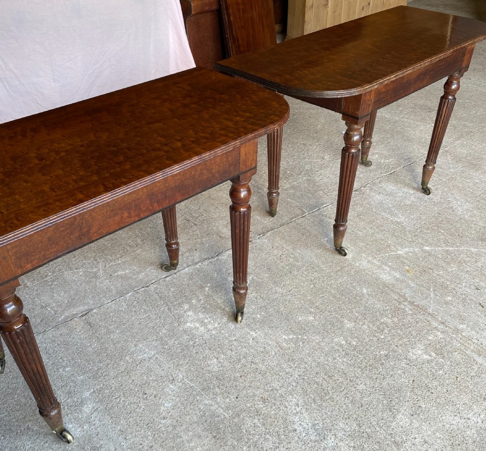 A pair of Regency mahogany console tables featuring rounded tops, reeded legs, and brass castors on a concrete surface. View IX