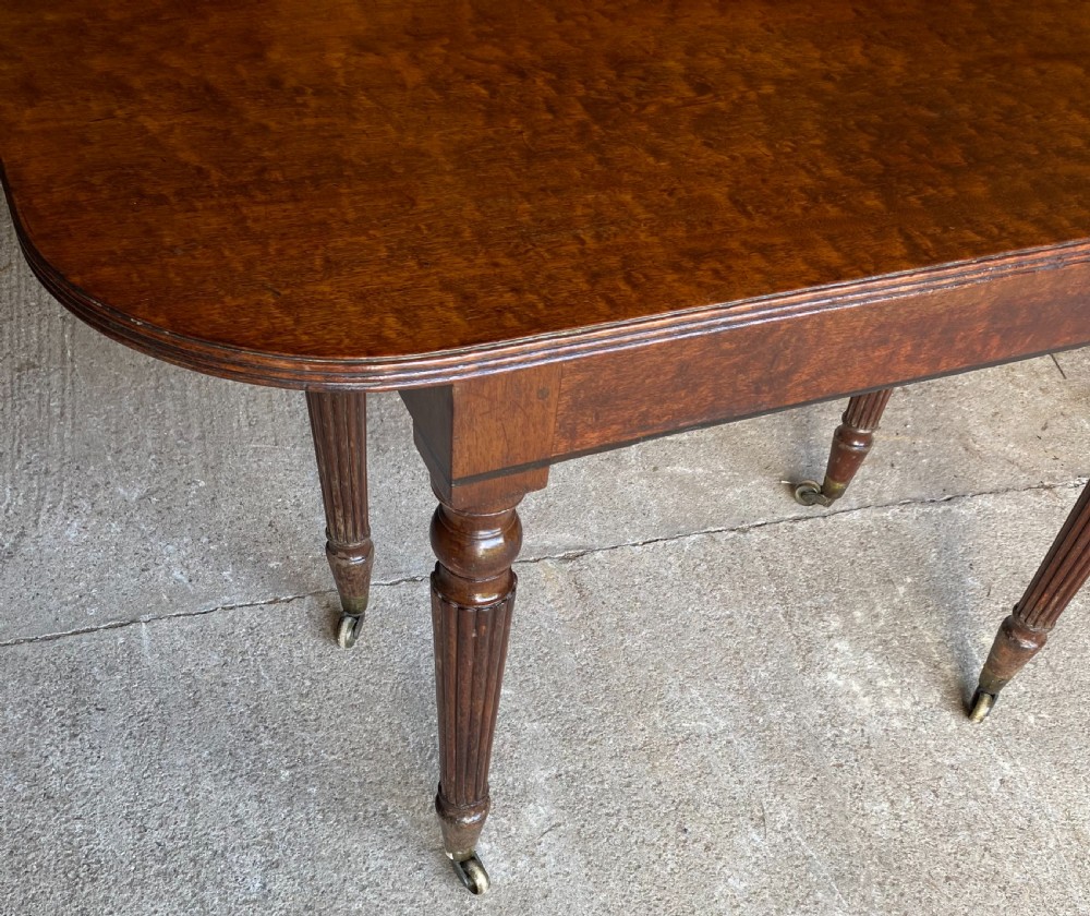 A pair of Regency mahogany console tables featuring rounded tops, reeded legs, and brass castors on a concrete surface. View X