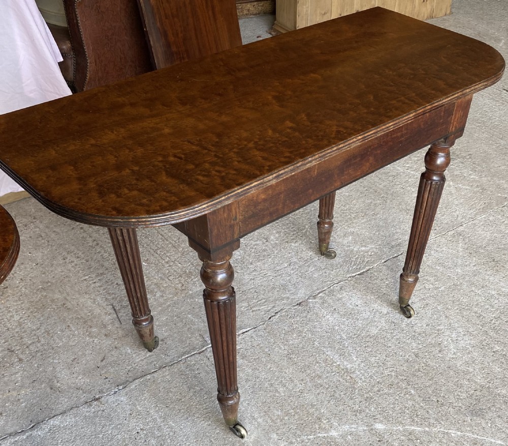 A pair of Regency mahogany console tables featuring rounded tops, reeded legs, and brass castors on a concrete surface. View XI