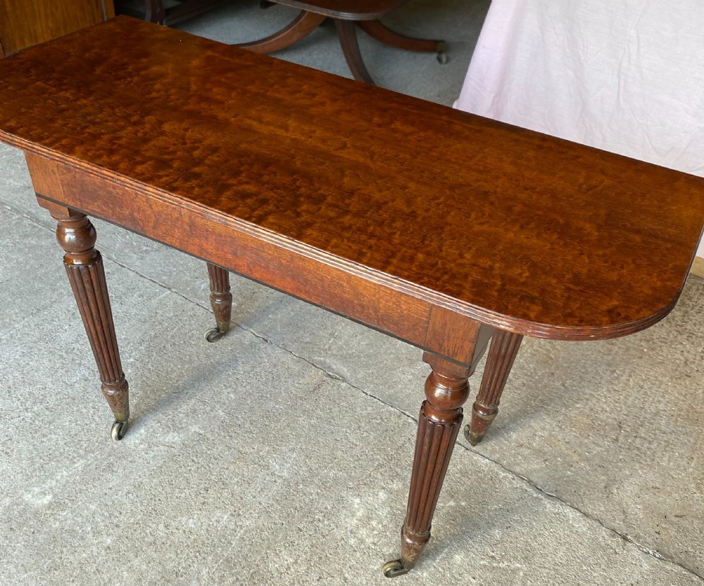 A pair of Regency mahogany console tables featuring rounded tops, reeded legs, and brass castors on a concrete surface. View XII