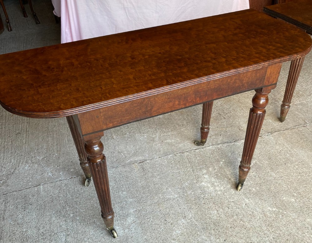 A pair of Regency mahogany console tables featuring rounded tops, reeded legs, and brass castors on a concrete surface. View XIII