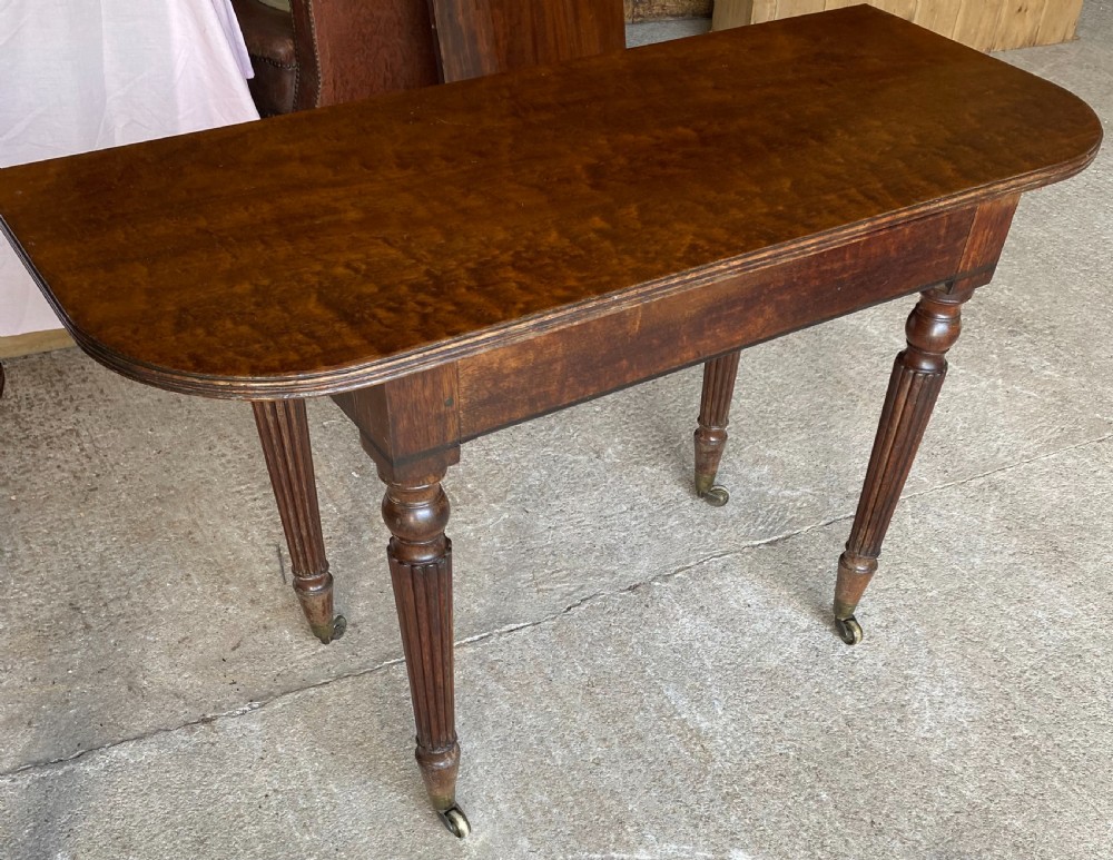 A pair of Regency mahogany console tables featuring rounded tops, reeded legs, and brass castors on a concrete surface. View XIV