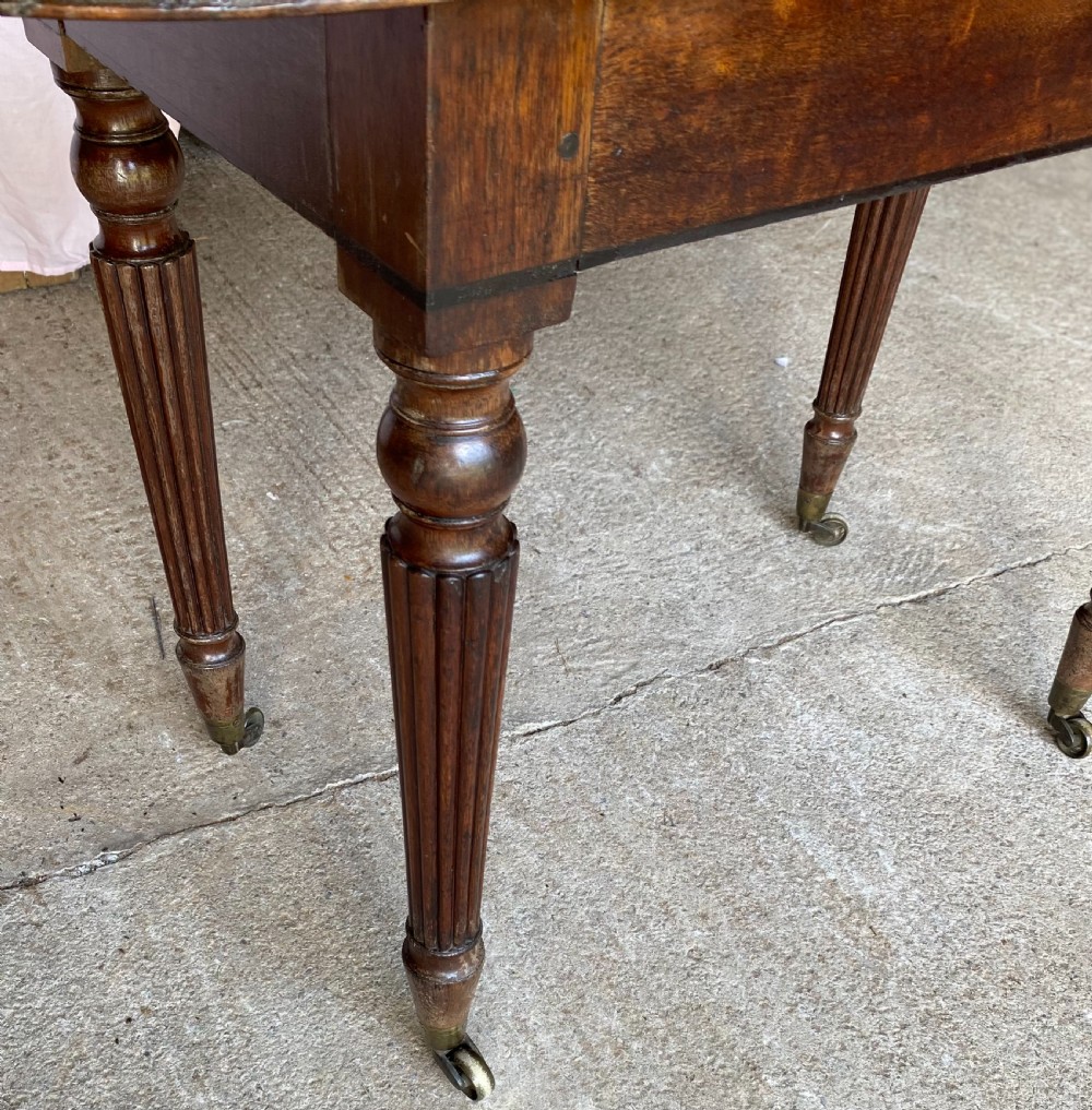 A pair of Regency mahogany console tables featuring rounded tops, reeded legs, and brass castors on a concrete surface. View XVI