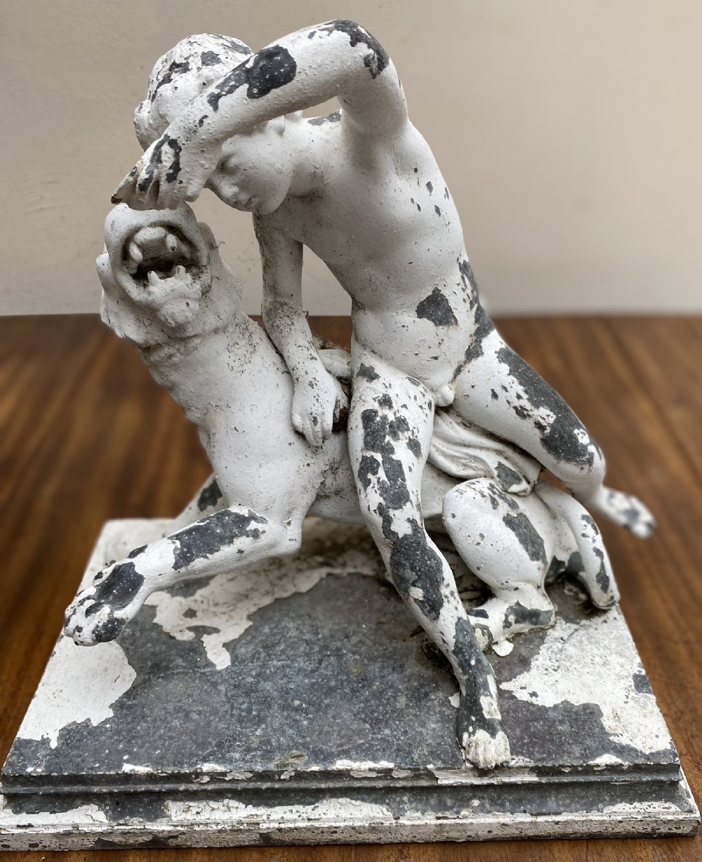 A classical cast metal sculpture depicting a seated youth leaning over a lion, featuring a heavily distressed white painted finish.
