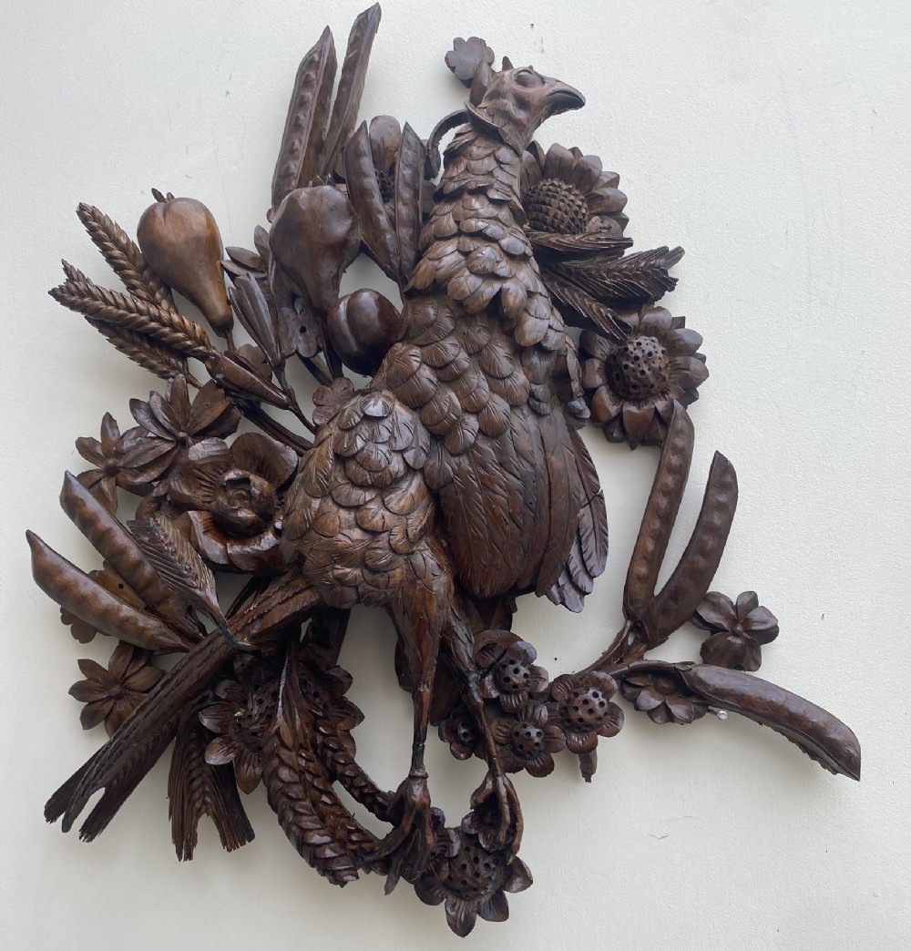A detailed high-relief dark timber wall plaque depicting a carved pheasant surrounded by wheat, sunflowers, and pod-like fruits.