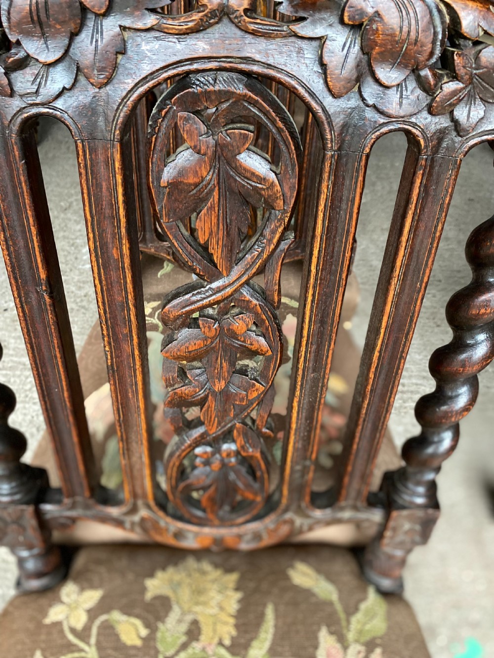 A dark carved oak dining chair featuring spiral turned legs, intricate leaf relief carvings on the backrest, and a beige upholstery seat with floral embroidery. View III