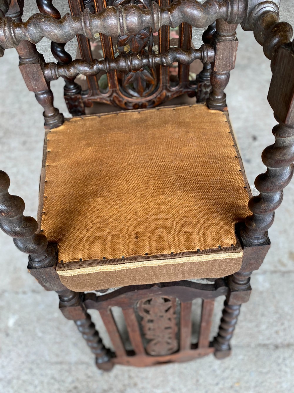 A dark carved oak dining chair featuring spiral turned legs, intricate leaf relief carvings on the backrest, and a beige upholstery seat with floral embroidery. View V