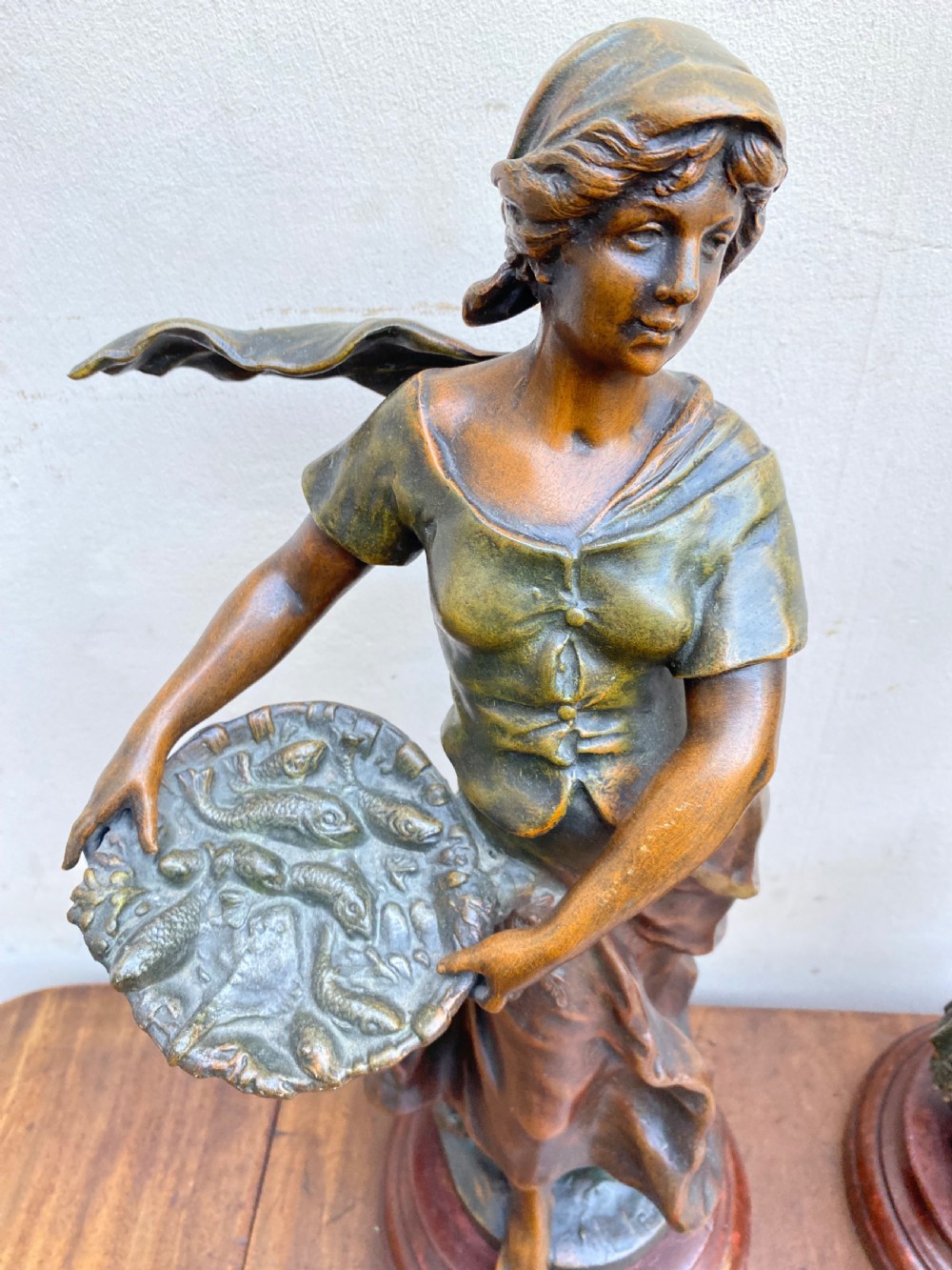 A pair of patinated spelter figures depicting a fisherwoman holding a basket and a fisherman carrying nets, mounted on circular turned wood bases with brass title plates. View II