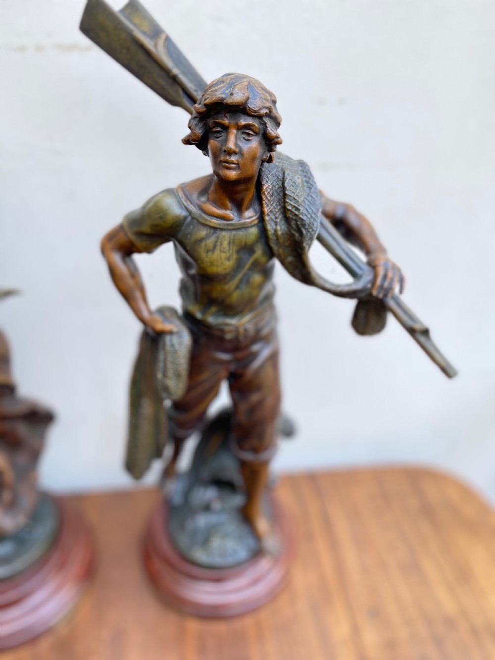 A pair of patinated spelter figures depicting a fisherwoman holding a basket and a fisherman carrying nets, mounted on circular turned wood bases with brass title plates. View III