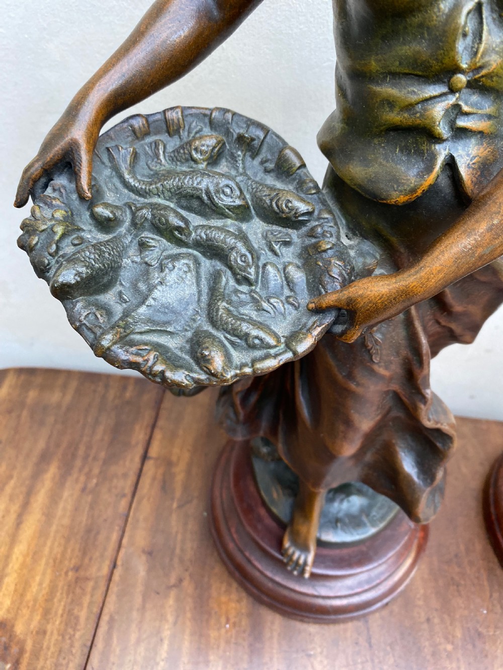 A pair of patinated spelter figures depicting a fisherwoman holding a basket and a fisherman carrying nets, mounted on circular turned wood bases with brass title plates. View IV