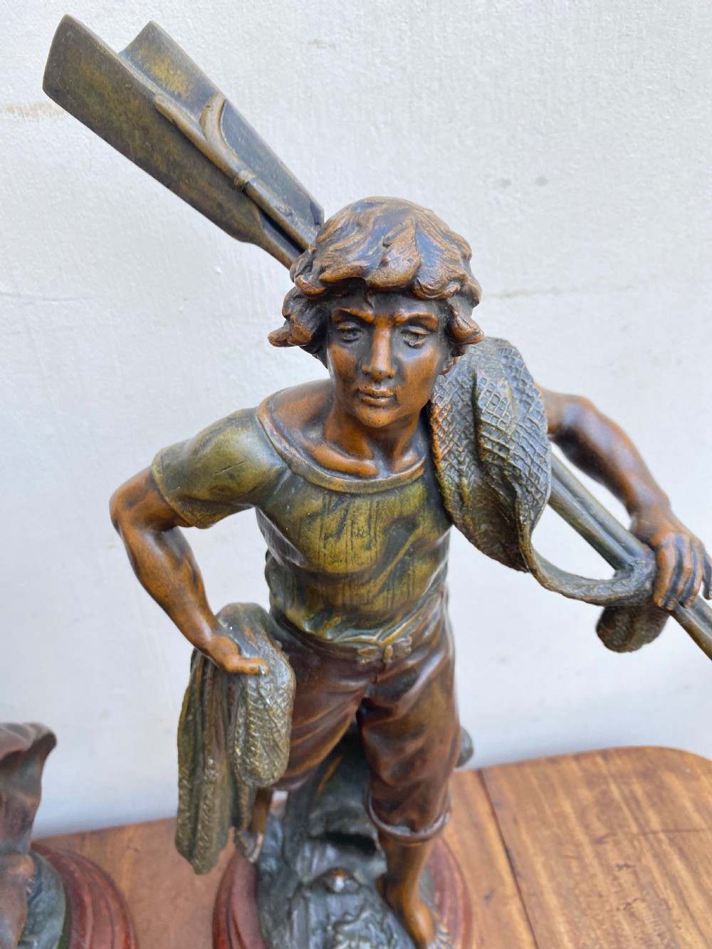 A pair of patinated spelter figures depicting a fisherwoman holding a basket and a fisherman carrying nets, mounted on circular turned wood bases with brass title plates. View V