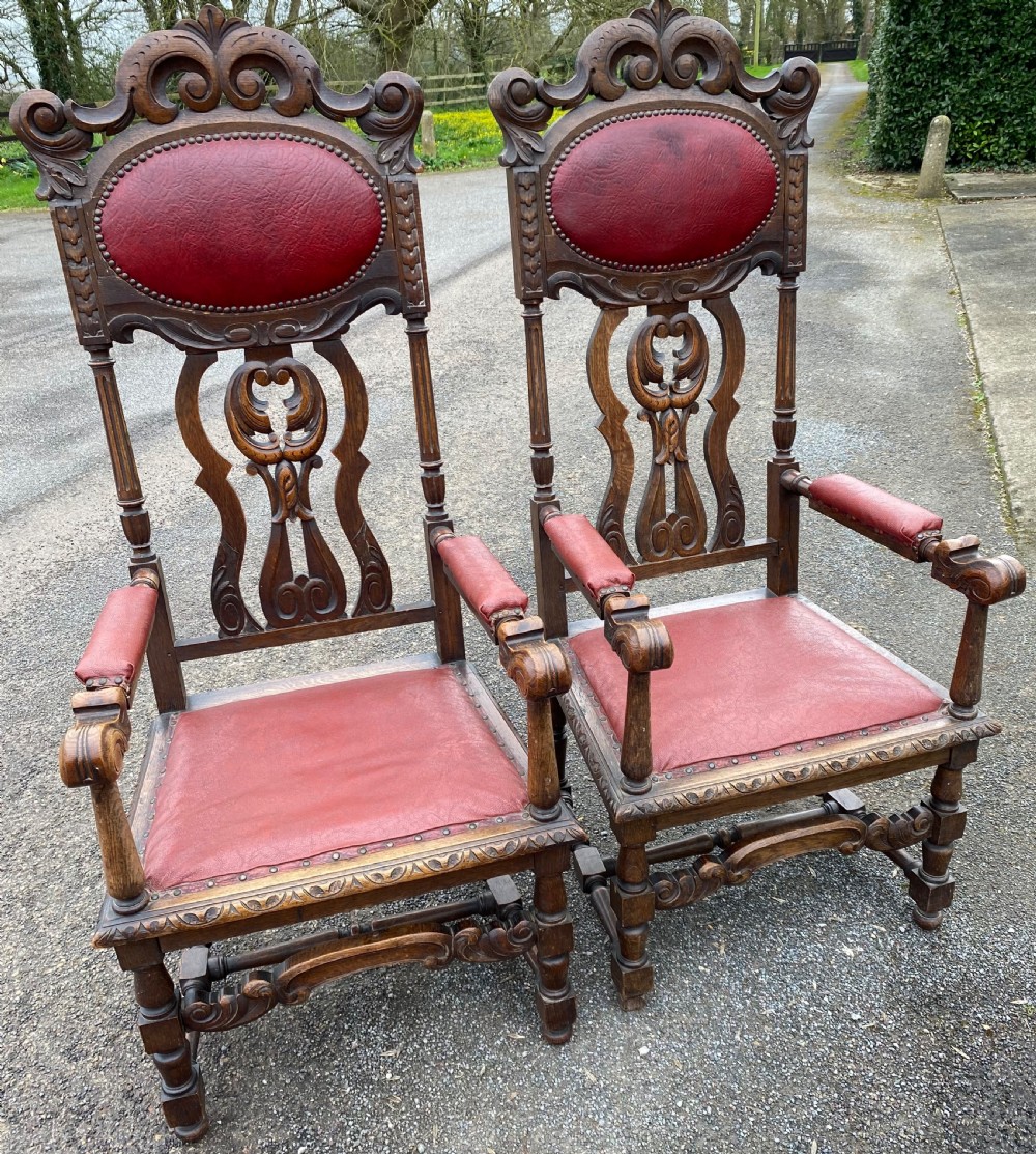 A pair of high-backed carved dark oak armchairs featuring red upholstered seats and matching oval back cushions.