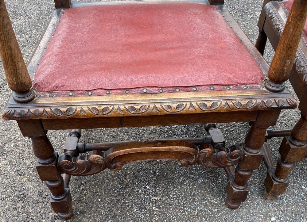 A pair of high-backed carved dark oak armchairs featuring red upholstered seats and matching oval back cushions. View III