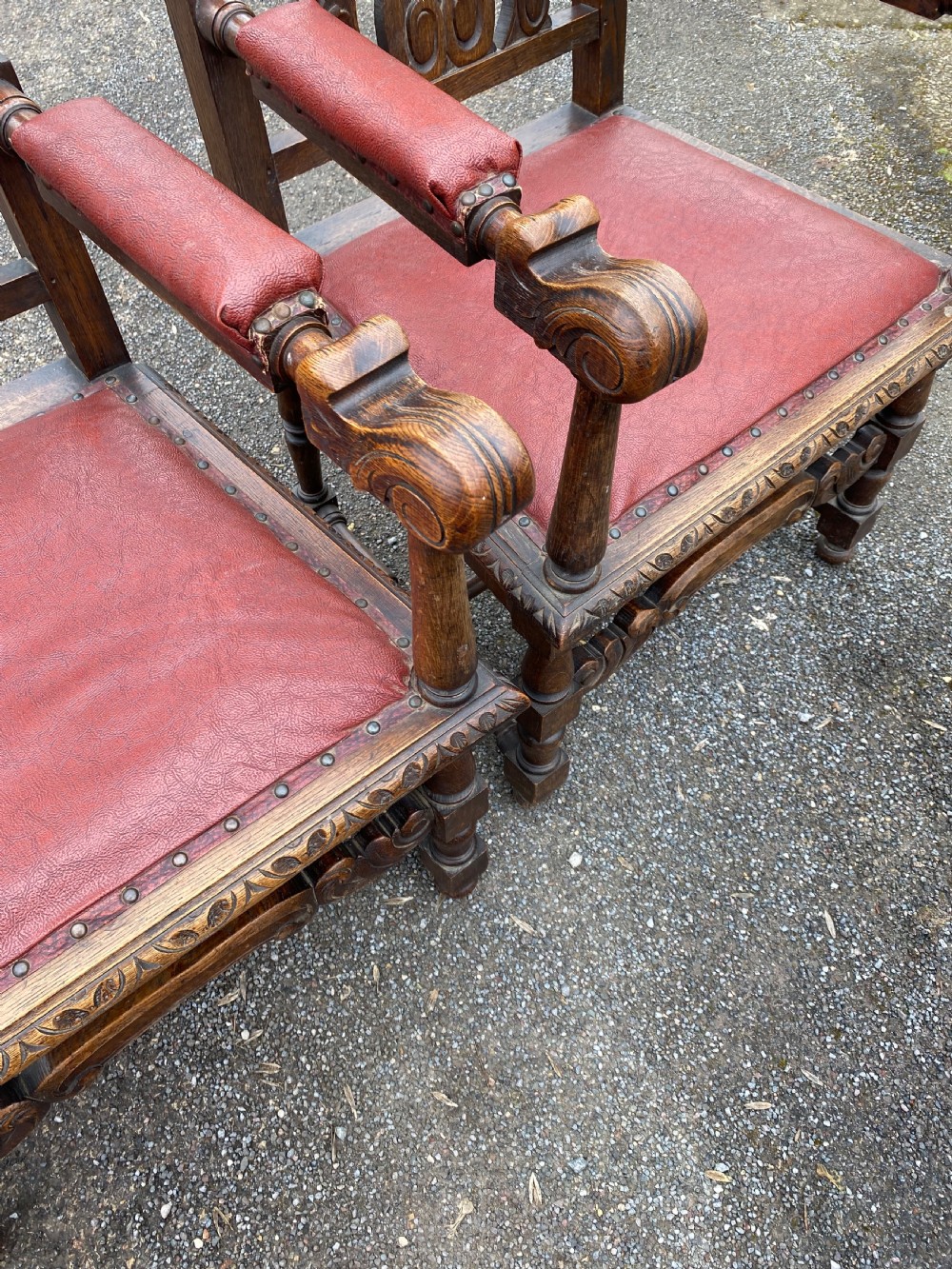 A pair of high-backed carved dark oak armchairs featuring red upholstered seats and matching oval back cushions. View IV