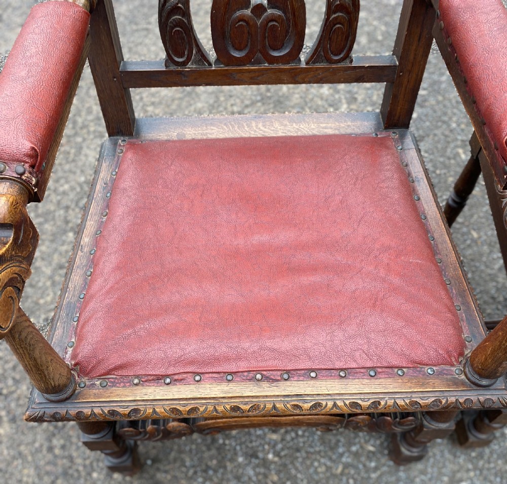 A pair of high-backed carved dark oak armchairs featuring red upholstered seats and matching oval back cushions. View V