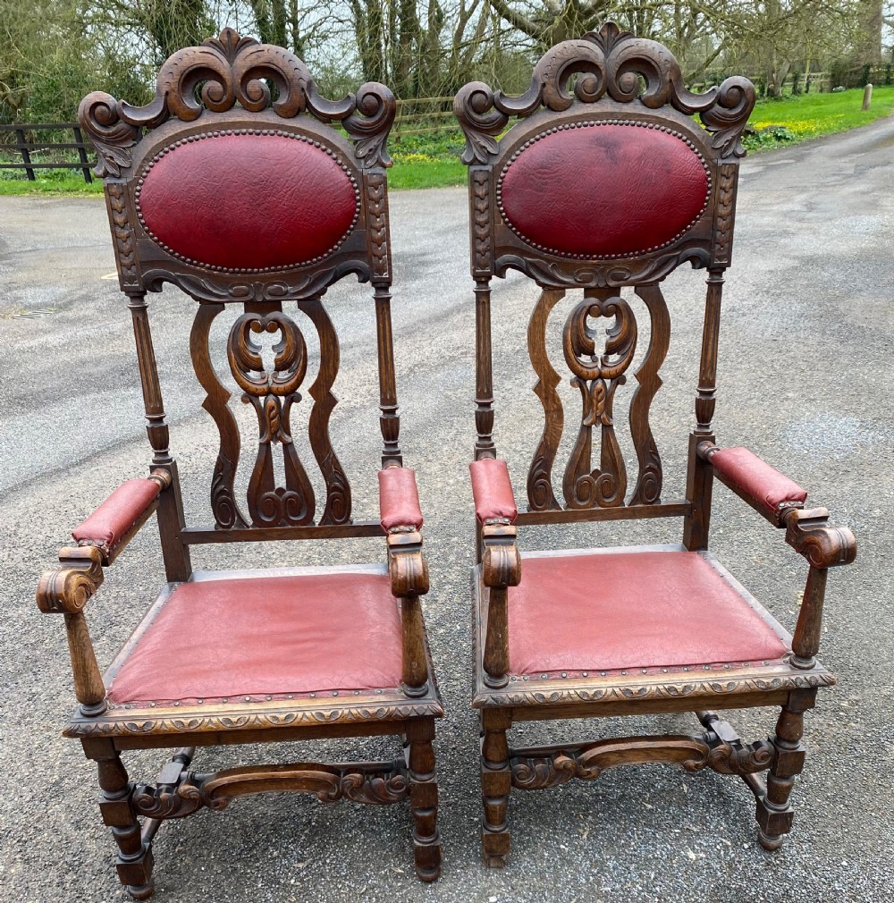 A pair of high-backed carved dark oak armchairs featuring red upholstered seats and matching oval back cushions. View VI