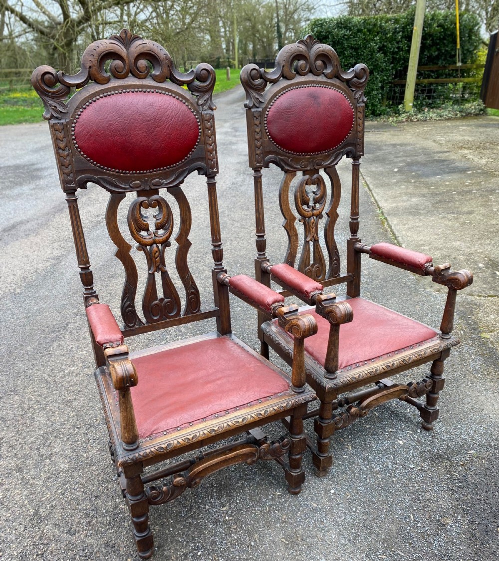 A pair of high-backed carved dark oak armchairs featuring red upholstered seats and matching oval back cushions. View VII