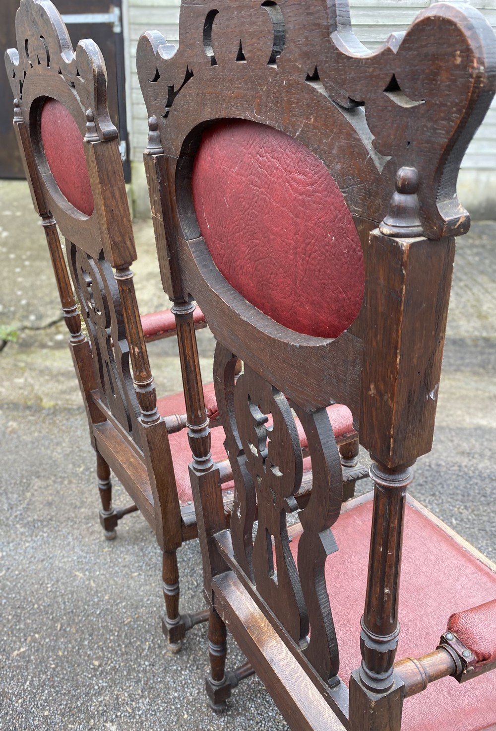 A pair of high-backed carved dark oak armchairs featuring red upholstered seats and matching oval back cushions. View VIII