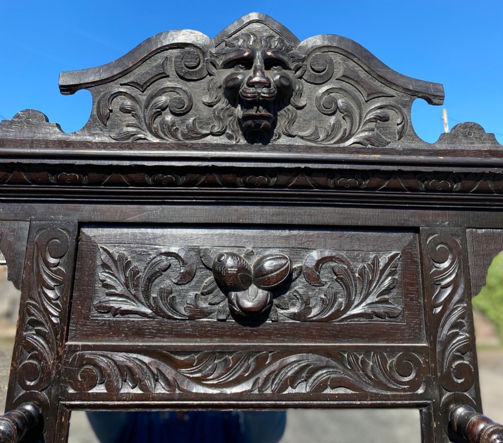 A dark carved oak Victorian hall stand featuring a central rectangular mirror, lion mask carvings, turned coat pegs, umbrella holders, and metal drip trays. View III