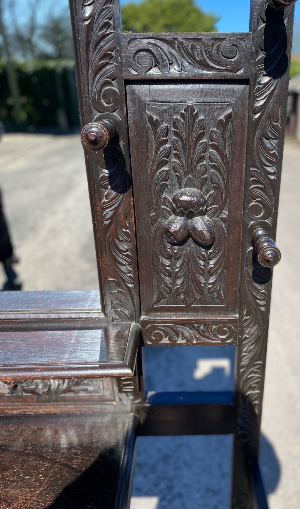 A dark carved oak Victorian hall stand featuring a central rectangular mirror, lion mask carvings, turned coat pegs, umbrella holders, and metal drip trays. View VI