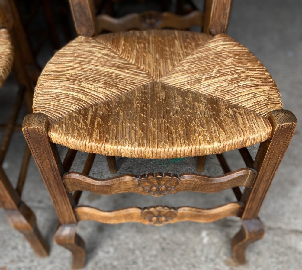 A set of French carved cedarwood dining chairs featuring ladderbacks with shell motifs and natural woven rush seats. View II