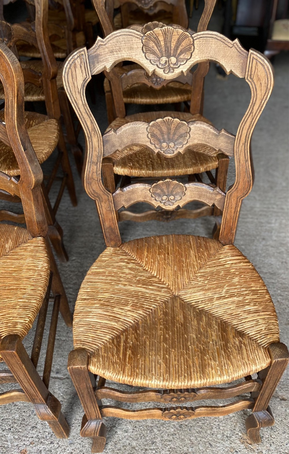 A set of French carved cedarwood dining chairs featuring ladderbacks with shell motifs and natural woven rush seats. View III