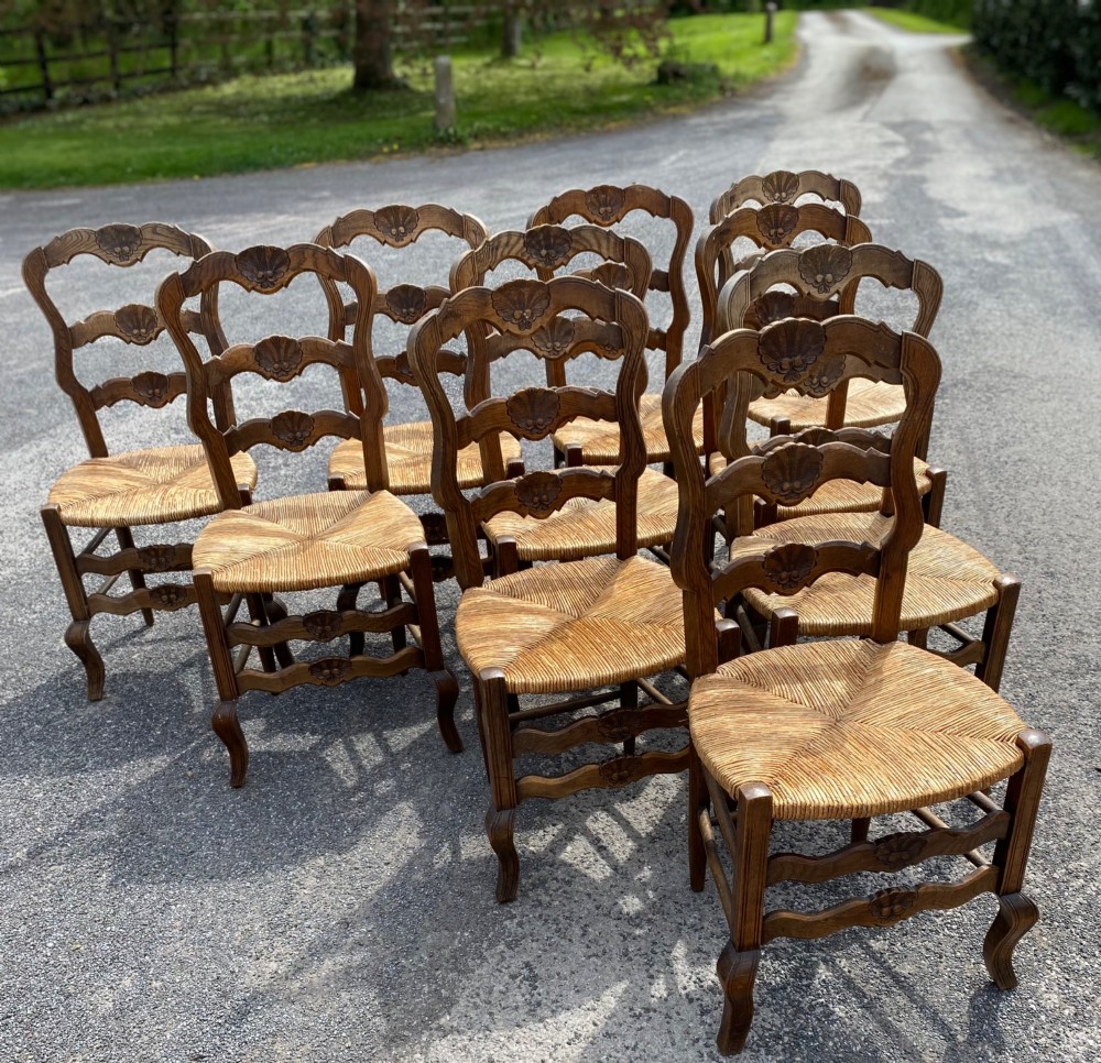 A set of French carved cedarwood dining chairs featuring ladderbacks with shell motifs and natural woven rush seats. View V