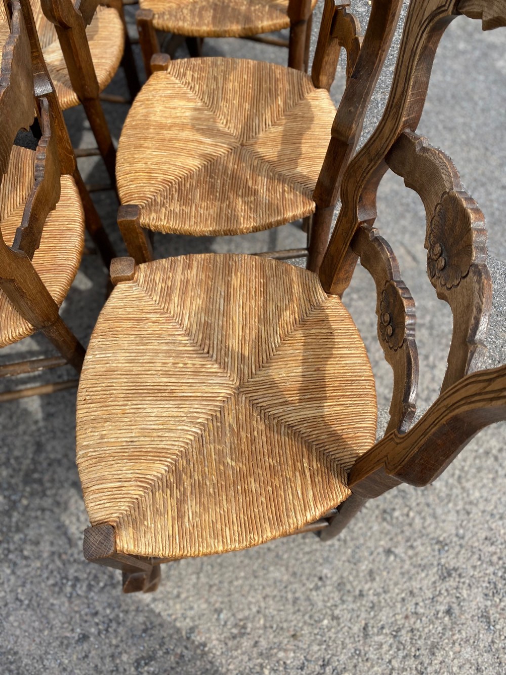 A set of French carved cedarwood dining chairs featuring ladderbacks with shell motifs and natural woven rush seats. View VII