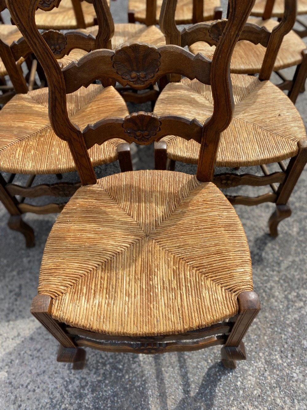 A set of French carved cedarwood dining chairs featuring ladderbacks with shell motifs and natural woven rush seats. View VIII